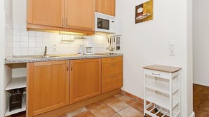 Una cocina con armarios de madera, microondas, cafetera y un carrito pequeño blanco.
