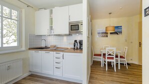 A modern kitchen with white cabinets, a microwave, and a dining area with white chairs and a table.