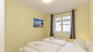 A bedroom with two beds, a window with curtains, a radiator, and a picture on the wall.