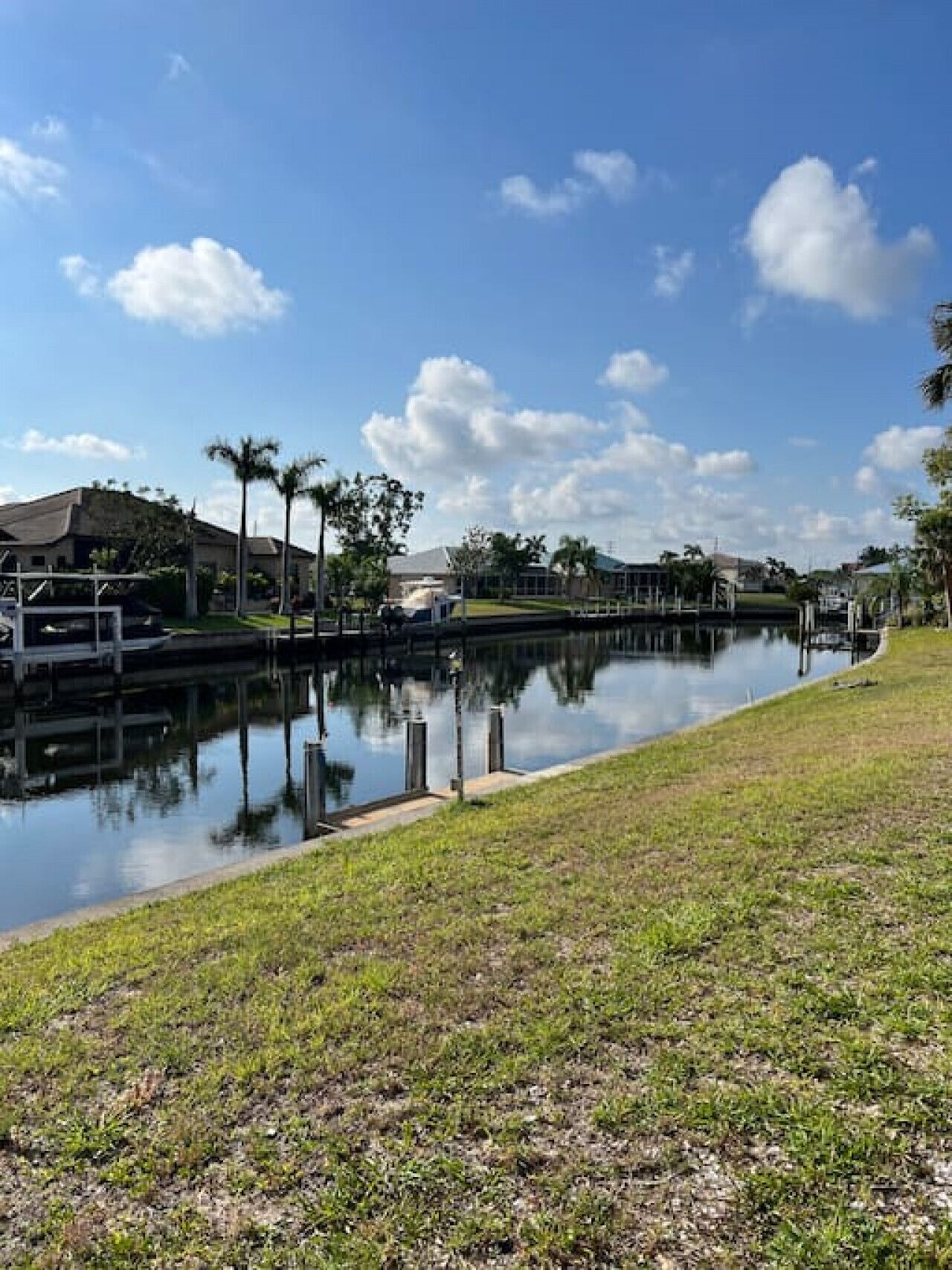 A calm waterway with a grassy bank, a pedestrian bridge, and residential buildings in the background.