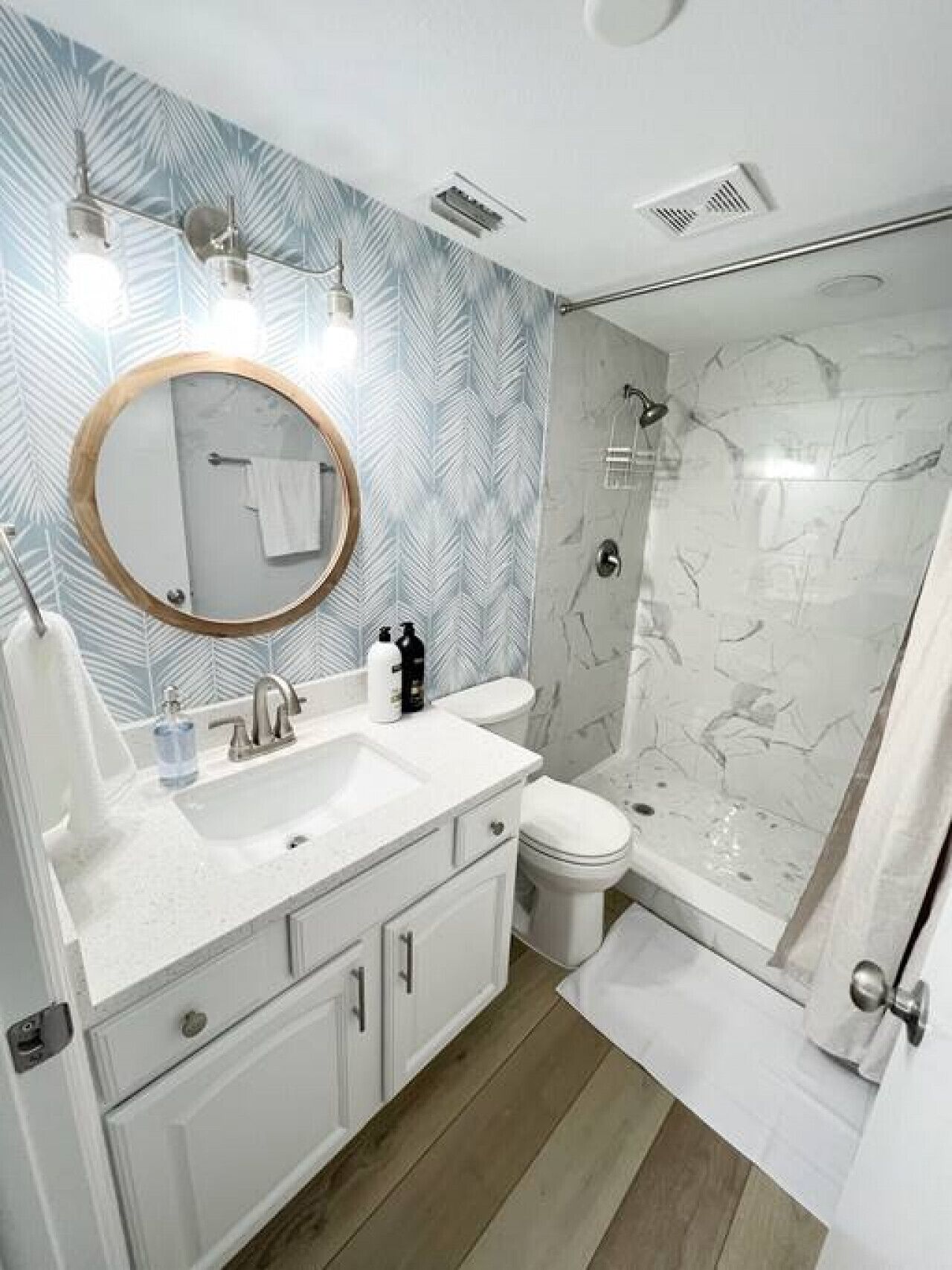 Une salle de bain avec un meuble-lavabo blanc, un miroir rond, des toilettes et un espace douche.