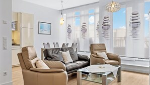 A modern living room with two leather sofas, a glass coffee table, and a kitchen area with a microwave.