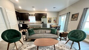Un salon moderne avec un canapé gris, deux fauteuils verts, une table basse en bois et un tapis à motifs.