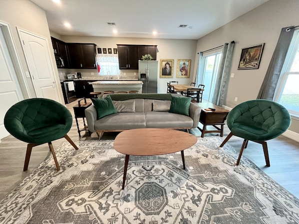 A modern living room with a grey sofa, two green armchairs, a wooden coffee table, and a patterned rug. - Sweet Stay in Sanford (Sanford)