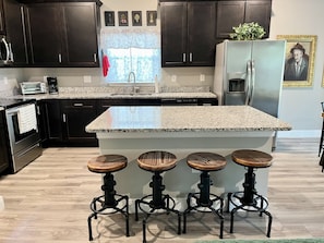 A modern kitchen with dark cabinets, a granite countertop, and a central island with stools. - Sweet Stay in Sanford (Sanford)