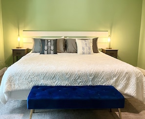 A neatly made bed with a white duvet, a blue bench, and multiple pillows. There are two bedside tables with lamps. - Sweet Stay in Sanford (Sanford)