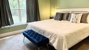 Une chambre à coucher avec un grand lit, un banc, une table de chevet et une fenêtre avec des rideaux.