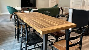 Un coin repas avec une table en bois et des chaises noires agrémentées de détails en laiton, un fauteuil vert recouvert de tissu, un téléviseur et des tableaux encadrés accrochés au mur.
