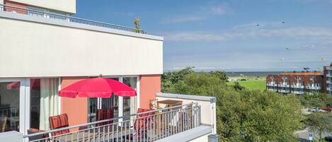 A balcony with outdoor furniture and a red umbrella, overlooking a residential area with trees and buildings.