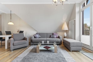 A modern living room with a grey sofa, a glass coffee table, and a dining area with a white table and chairs.