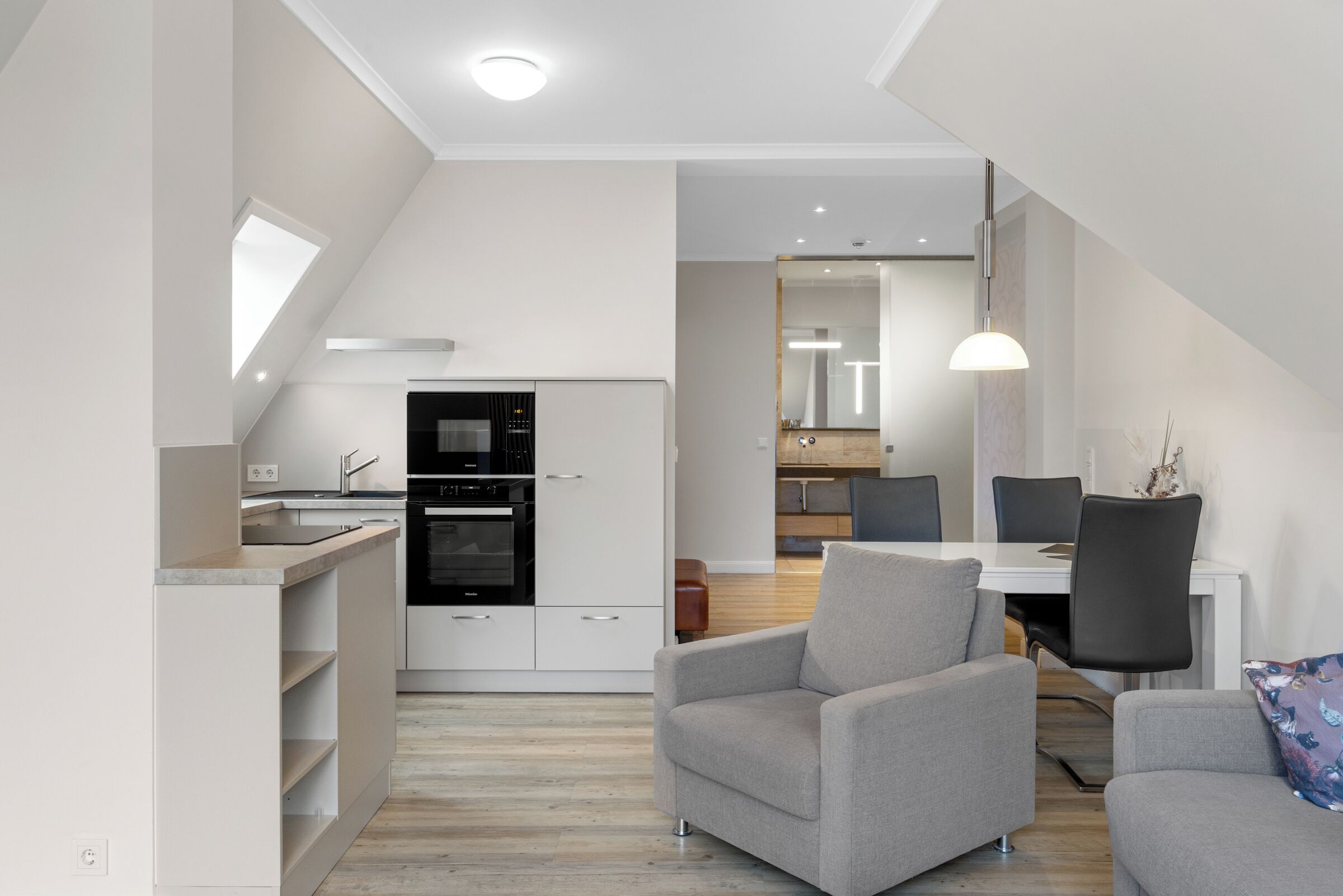 A modern kitchen with built-in appliances, a dining area with a table and chairs, and a staircase leading to an upper level.