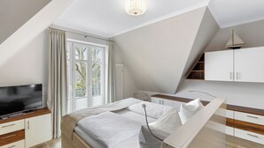 A modern bedroom with a bed, a TV, a desk, and a window.