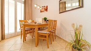 Un comedor con una mesa y sillas de madera, una lámpara colgante, un espejo en la pared y una planta en maceta.