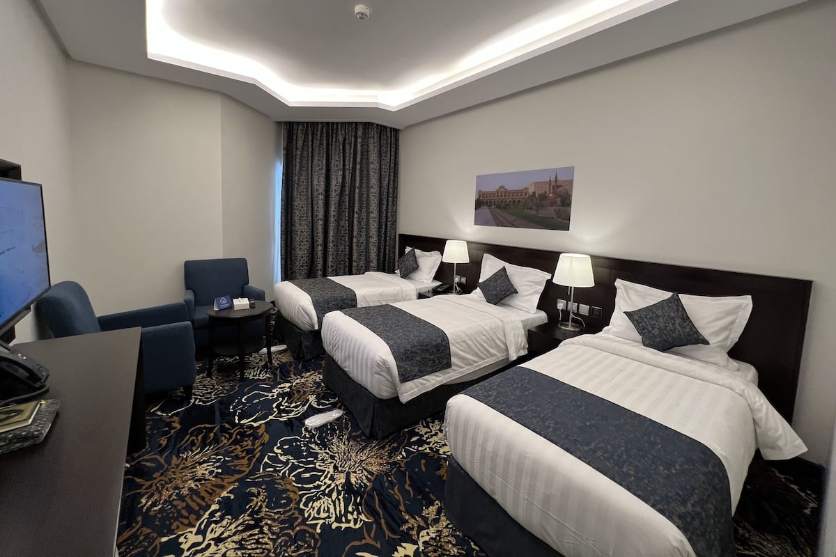 Habitación de hotel con dos camas, un escritorio, una silla y un televisor.