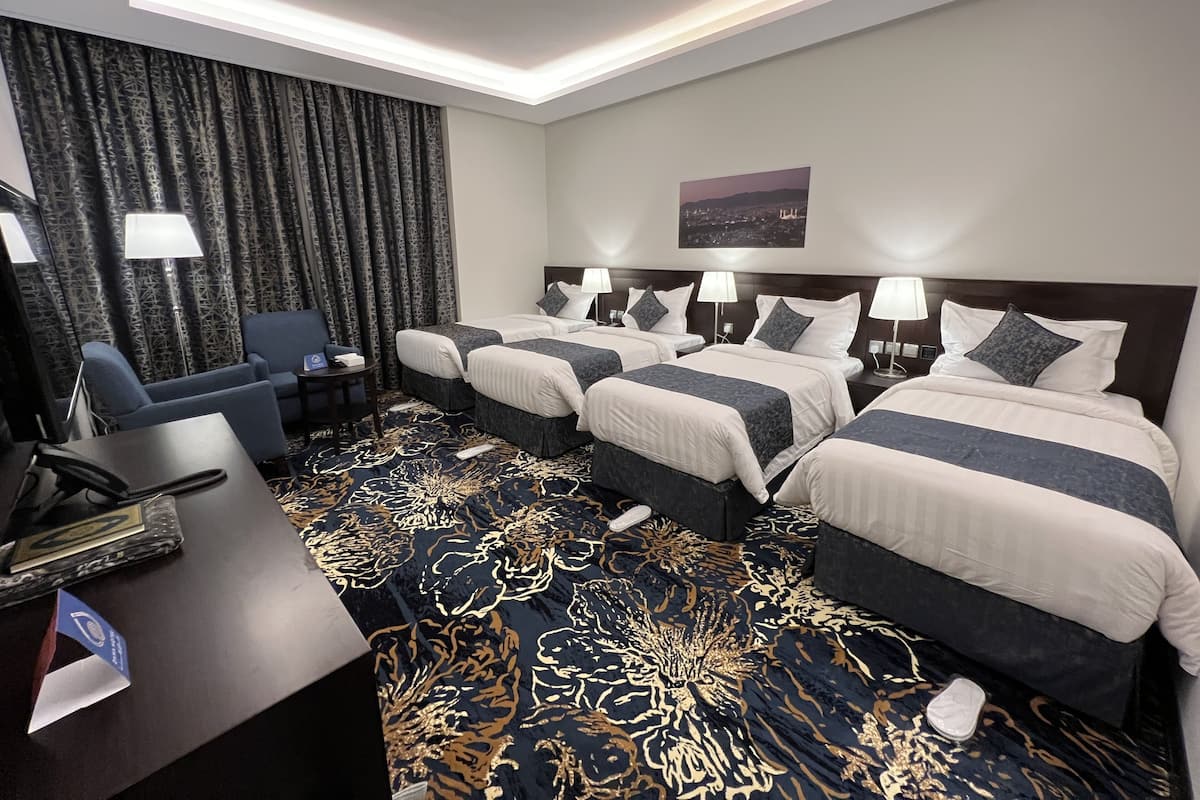 Habitación de hotel con dos camas, un escritorio, una silla y un ventanal grande con cortinas.