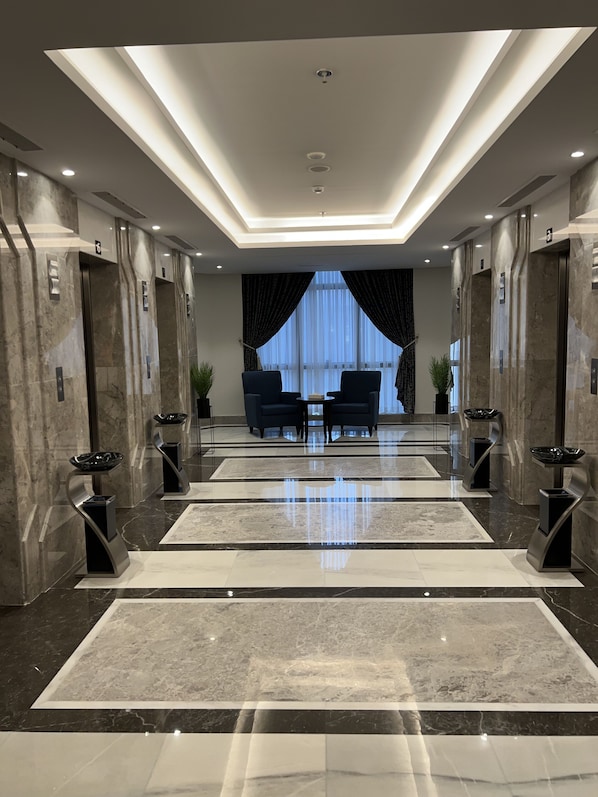 Een moderne lobby met marmeren vloeren, twee banken en een groot raam met gordijnen.