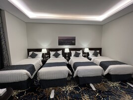 Habitación de hotel con cuatro camas dispuestas en fila, vista panorámica de la ciudad y alfombra estampada.