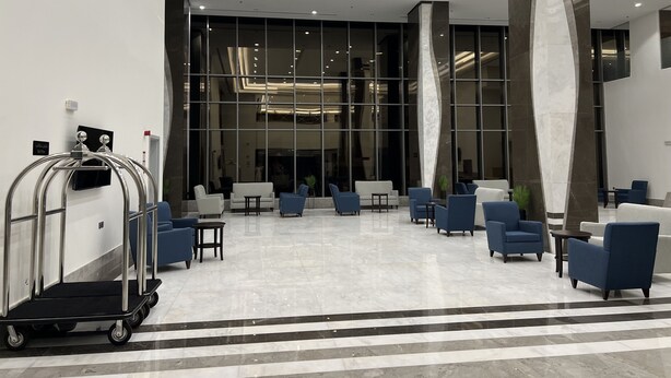 A spacious lobby with a modern design, featuring a seating area with blue and white chairs, a reception desk, and a large glass wall providing a view of the interior. - Zaha Taiba Hotel (Madinah)