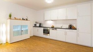 A modern kitchen with white cabinets, a wooden countertop, and a built-in oven. - Modernes, Strandnahes Apartment mit Großem Balkon, Fußbodenheizung u. Kaminofen (Ostseebad Binz)