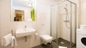 A modern bathroom with a glass shower enclosure, a sink, a toilet, and a washing machine. - Modernes, Strandnahes Apartment mit Großem Balkon, Fußbodenheizung u. Kaminofen (Ostseebad Binz)