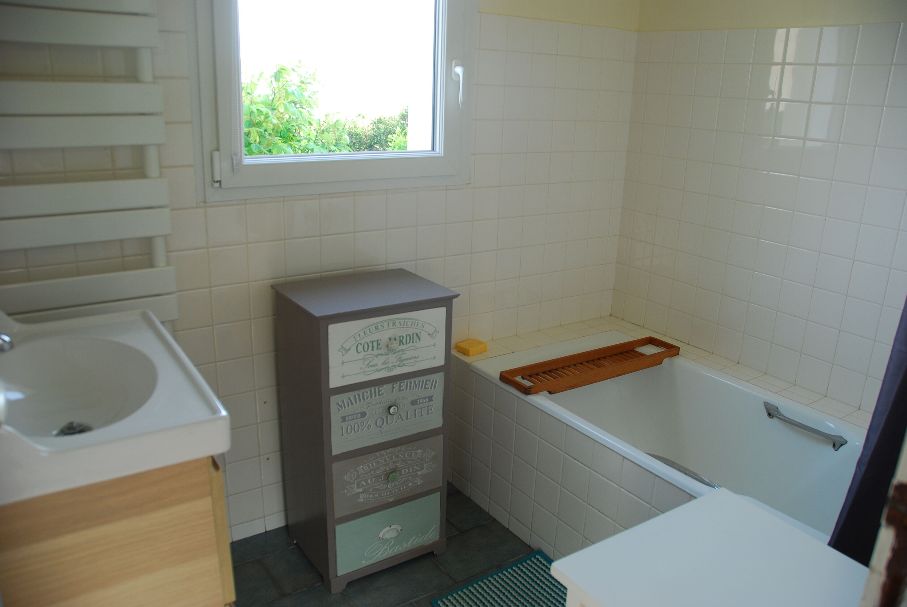 A bathroom with a sink, a vanity with drawers, a bathtub, and a window.