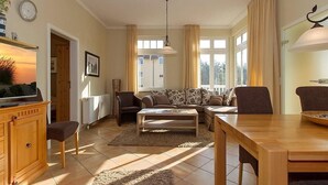 Una sala de estar con un sofá, sillas, una mesa de centro, un televisor y una mesa de comedor.