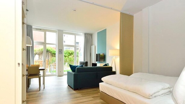 A hotel room with a bed, a sofa, a TV, and a dining area with a table and chairs.