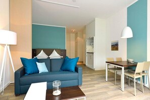 A modern living room with a sofa, coffee table, and dining table. - Tolles Apartment am Inselstrand mit Sonniger Terrasse - Meeresrauschen Inklusive (Nordseeheilbad Wangerooge)