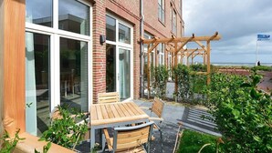 A patio with a wooden table and chairs, a pergola, and a view of the sea.