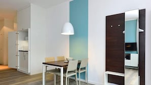 A modern dining area with a wooden table and chairs, a white pendant light, and a partially open wardrobe with a mirror.