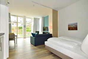 A modern hotel room with a large bed, a sofa, a TV, and a dining area with a table and chairs. - Tolles Apartment am Inselstrand mit Sonniger Terrasse - Meeresrauschen Inklusive (Nordseeheilbad Wangerooge)