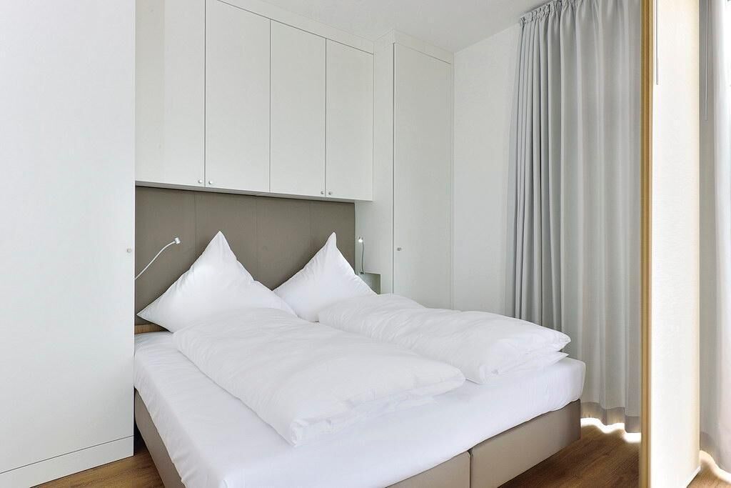 Une chambre moderne avec un lit, des rideaux blancs et une tête de lit de couleur claire.
