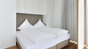 A modern bedroom with a bed, white curtains, and a light-colored headboard. - Tolles Ferienapartment am Inselstrand mit Meerblick, Balkon und Strandkorb! (Nordseeheilbad Wangerooge)