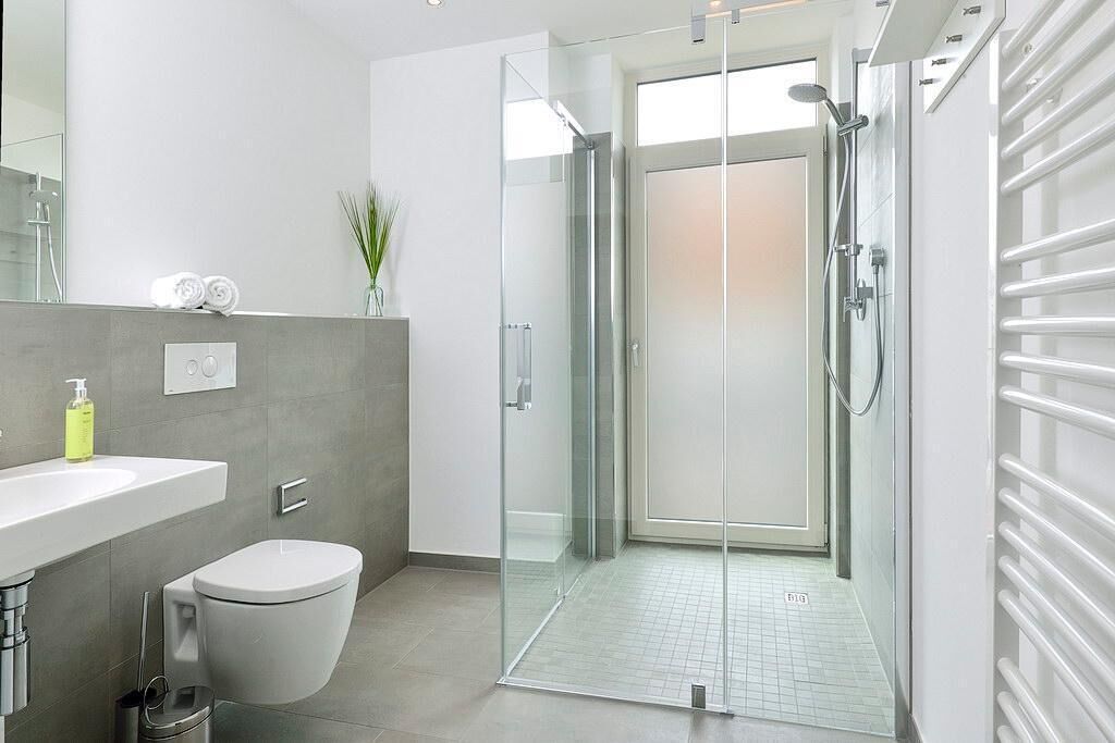 A modern bathroom with a glass shower enclosure, a toilet, a sink, and a towel rack.