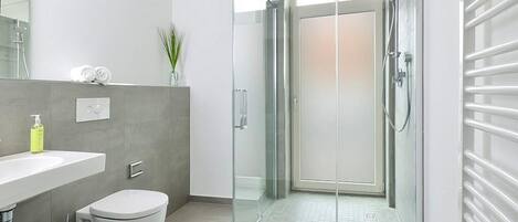A modern bathroom with a glass shower enclosure, a toilet, a sink, and a towel rack.