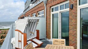 A balcony with wicker chairs and a table, overlooking the sea. - Tolles Ferienapartment am Inselstrand mit Meerblick, Balkon und Strandkorb! (Nordseeheilbad Wangerooge)