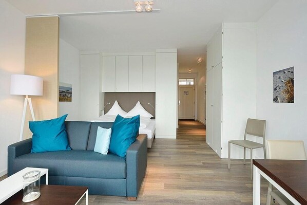 Una habitación de hotel moderna con un sofá gris, una cama con cabecera gris, un escritorio blanco y una silla.
