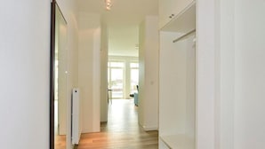 A hallway with a radiator, a white door, and a view into a living area with a sofa and a window.