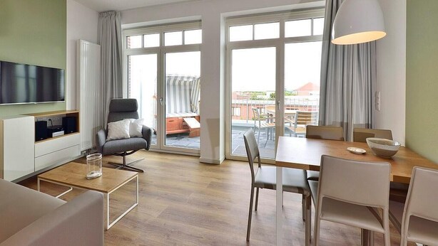 Un salon moderne doté d’un téléviseur à écran plat, d’un canapé, d’une table à manger avec des chaises et d’une grande fenêtre avec des rideaux.