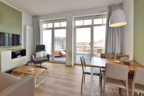 Uma sala de estar moderna com televisão de tela plana, sofá, mesa de jantar com cadeiras e uma grande janela com cortinas.