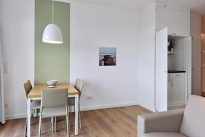 A dining area with a wooden table, white chairs, a white pendant light, and a small framed picture on the wall.