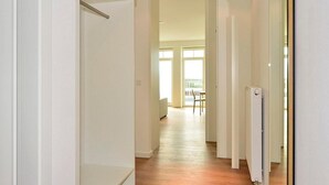 Un couloir lumineux avec un radiateur, une chaise et une vue sur un balcon à travers une porte vitrée.