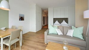 Un salon moderne avec un canapé, une table à manger et une table basse. On aperçoit un coin cuisine à l’arrière-plan.