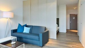 Ein modernes Wohnzimmer mit einer Couch, einer Stehlampe und einem Glas auf einem Beistelltisch.