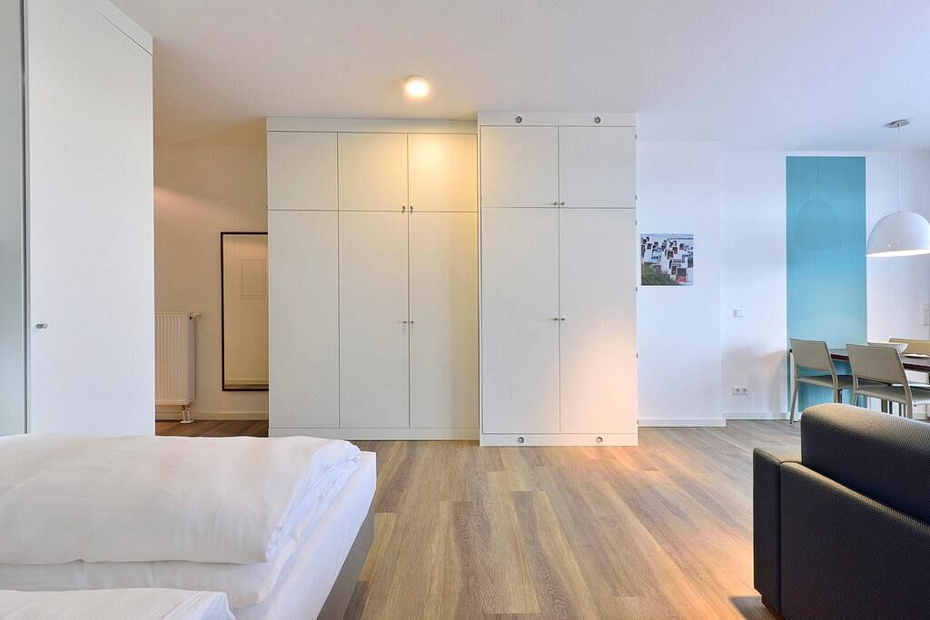 Ein modernes Hotelzimmer mit einem Bett, einer Sitzecke mit Tisch und einem Kleiderschrank mit mehreren Fächern.