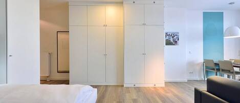 Ein modernes Hotelzimmer mit einem Bett, einer Sitzecke mit Tisch und einem Kleiderschrank mit mehreren Fächern.