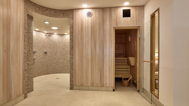 Ein moderner Wellnessbereich mit einer gebogenen Dusche, Holzpaneele und einer Holzauszeit.