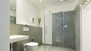 Ein modernes Badezimmer mit einer gläsernen Duschkabine, einem weißen Waschbecken und einer Toilette.