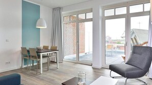 Ein modernes Wohnzimmer mit Essbereich, großen Schiebeglastüren zu einer Außenpatio und Blick auf ein Backsteingebäude.