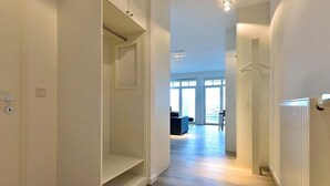Un pasillo con un radiador, una puerta que da a una habitación y vistas a un salón con un sofá y una mesa.